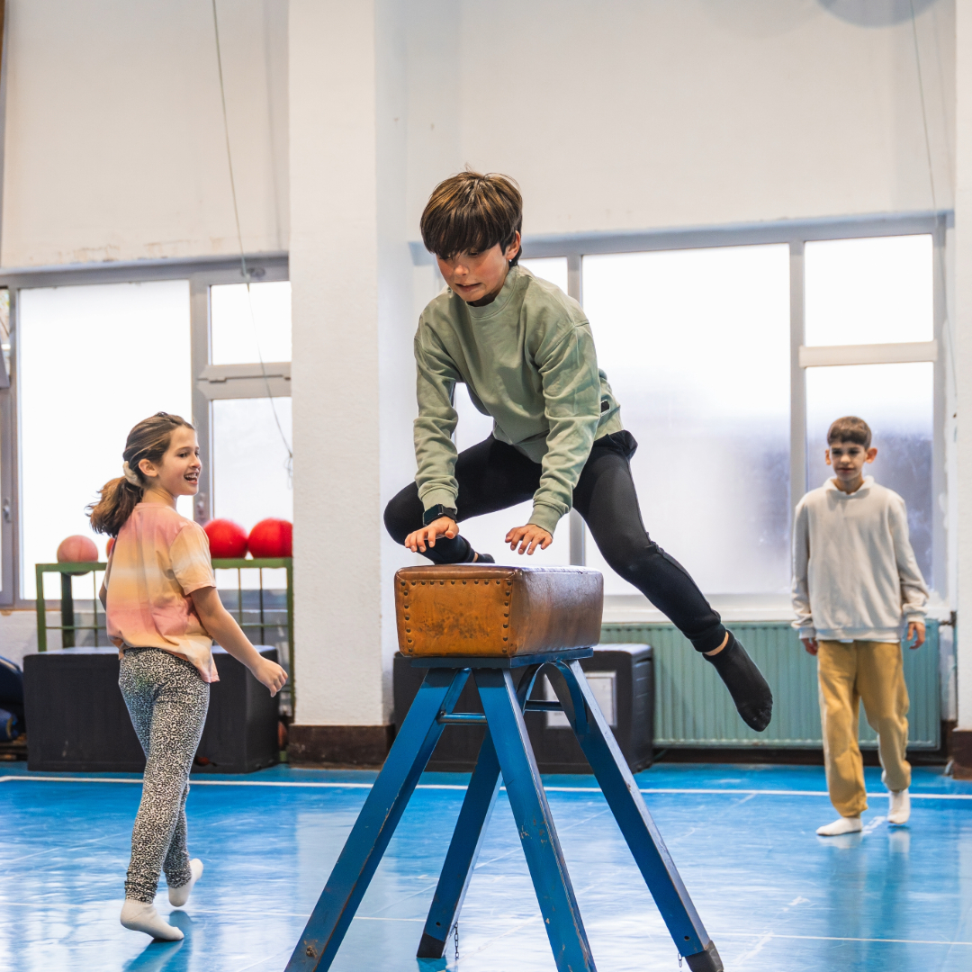 Children in a gymnastics session. A young boy is jumping on a balance beam.