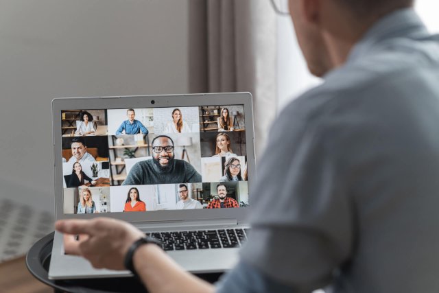 A person is engaging in an online classroom with a diverse group of people displayed on the laptop screen