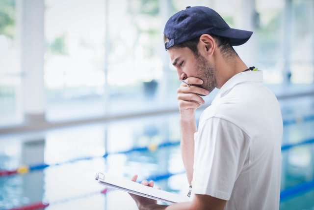Swimming coach holding clipboard at the pool pondering his notes