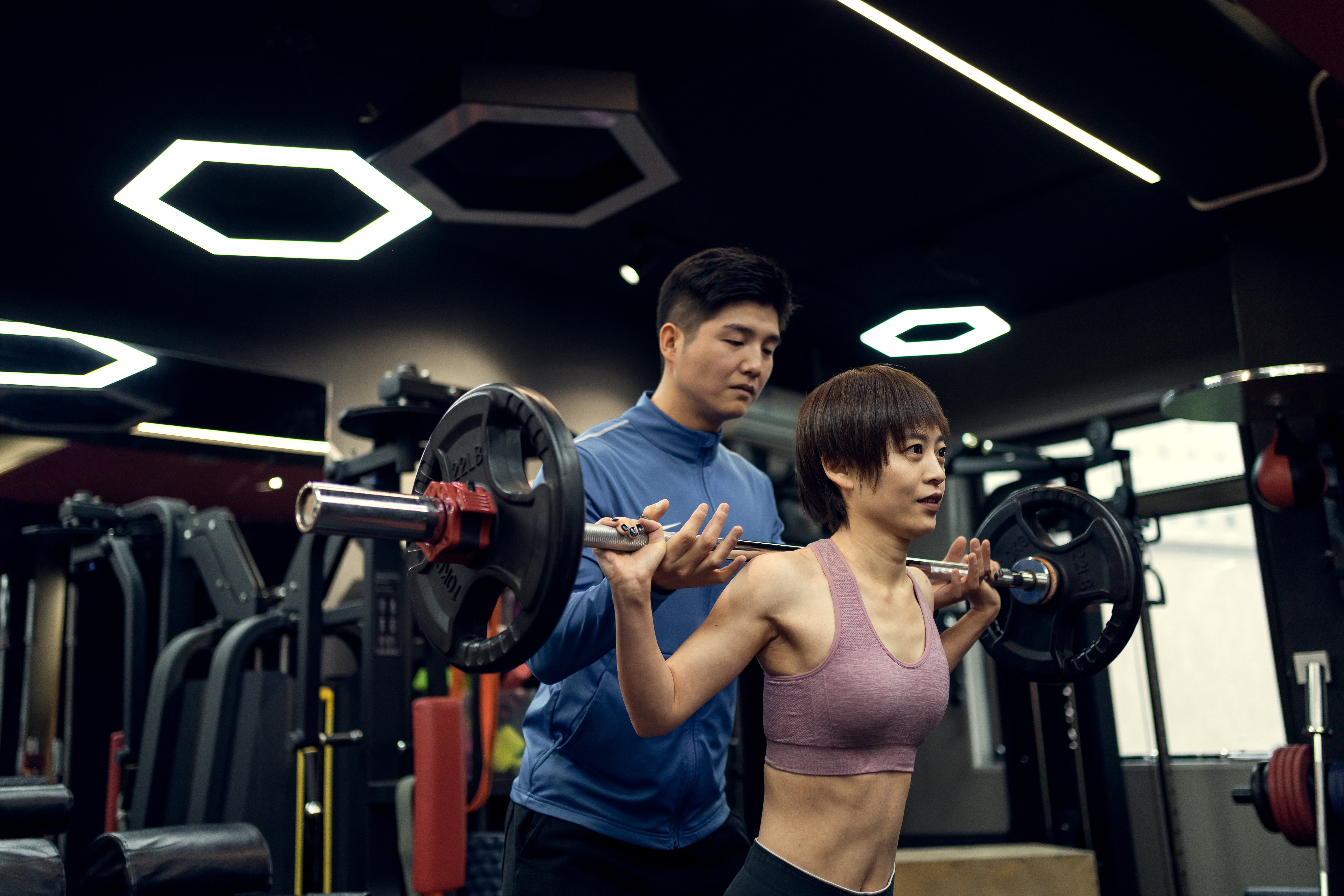 A coach works with his participant to help her perform a squat with a bell bar