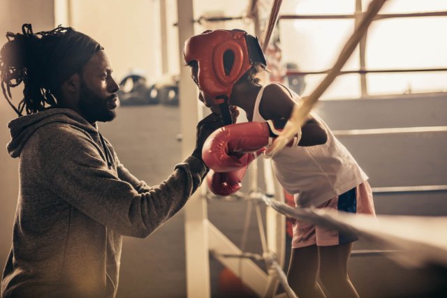 A boxing coach carefully ties a head guard onto a young boxer, preparing them for a fight, with focus and determination visible on their faces
