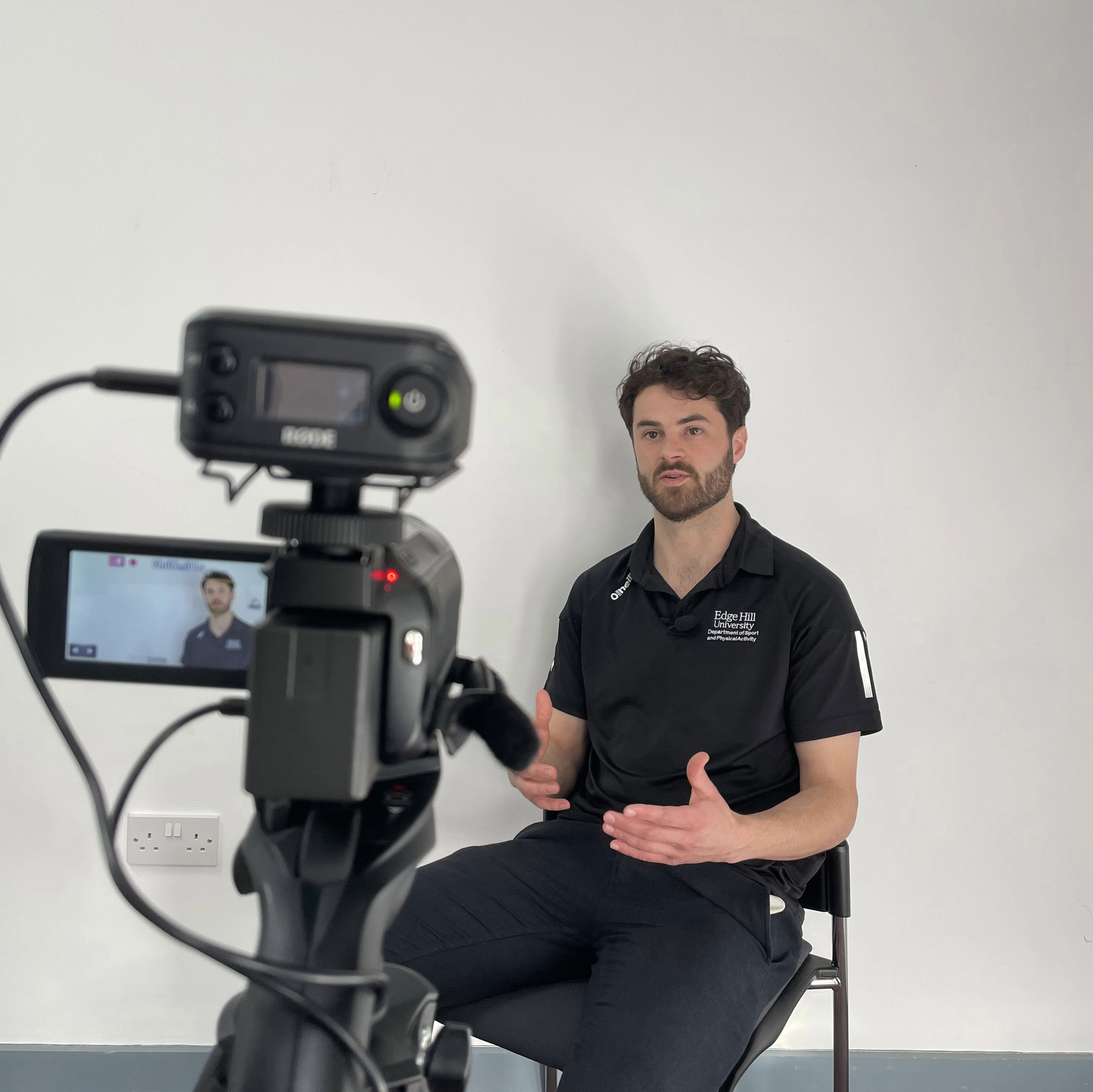 A coach sits in front of a video camera delivering a speech.