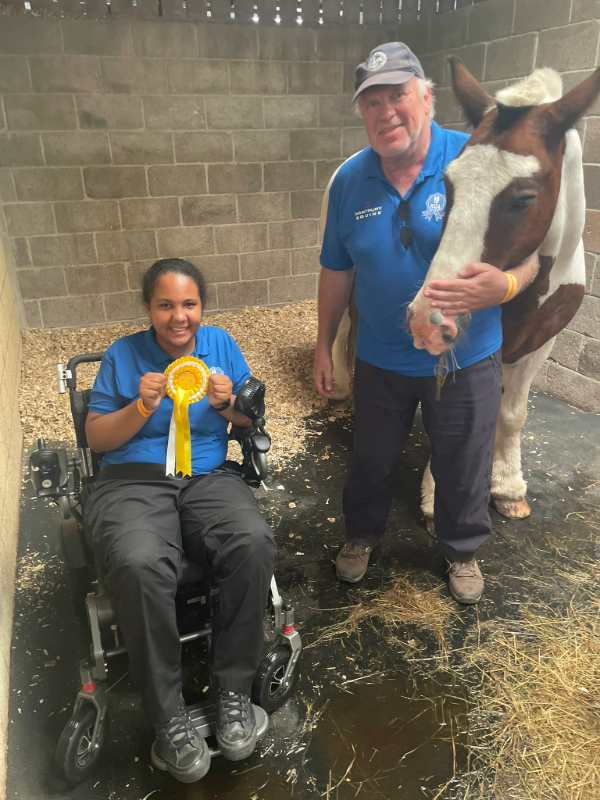 Lauryn Miller holds a yellow rosette alongside coach Peter Tomlin and horse Frankie