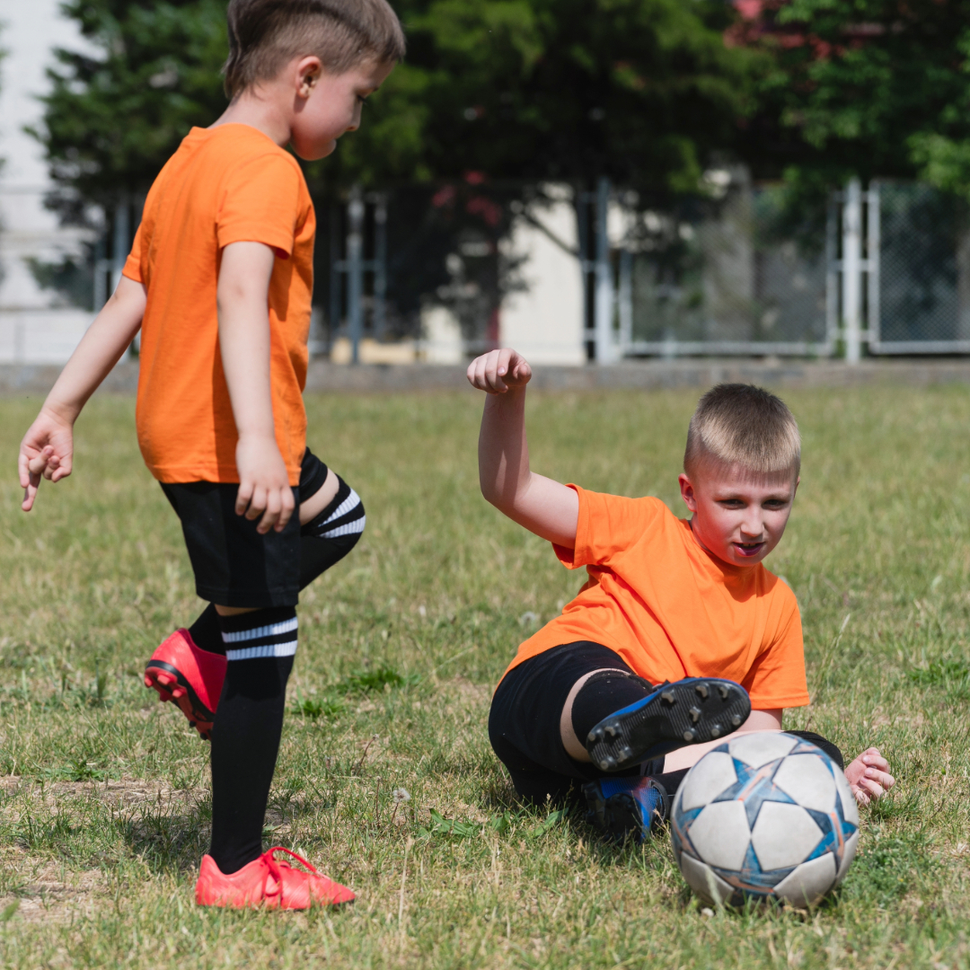 Two young boys play football. One on the right is doing a slide tackle.