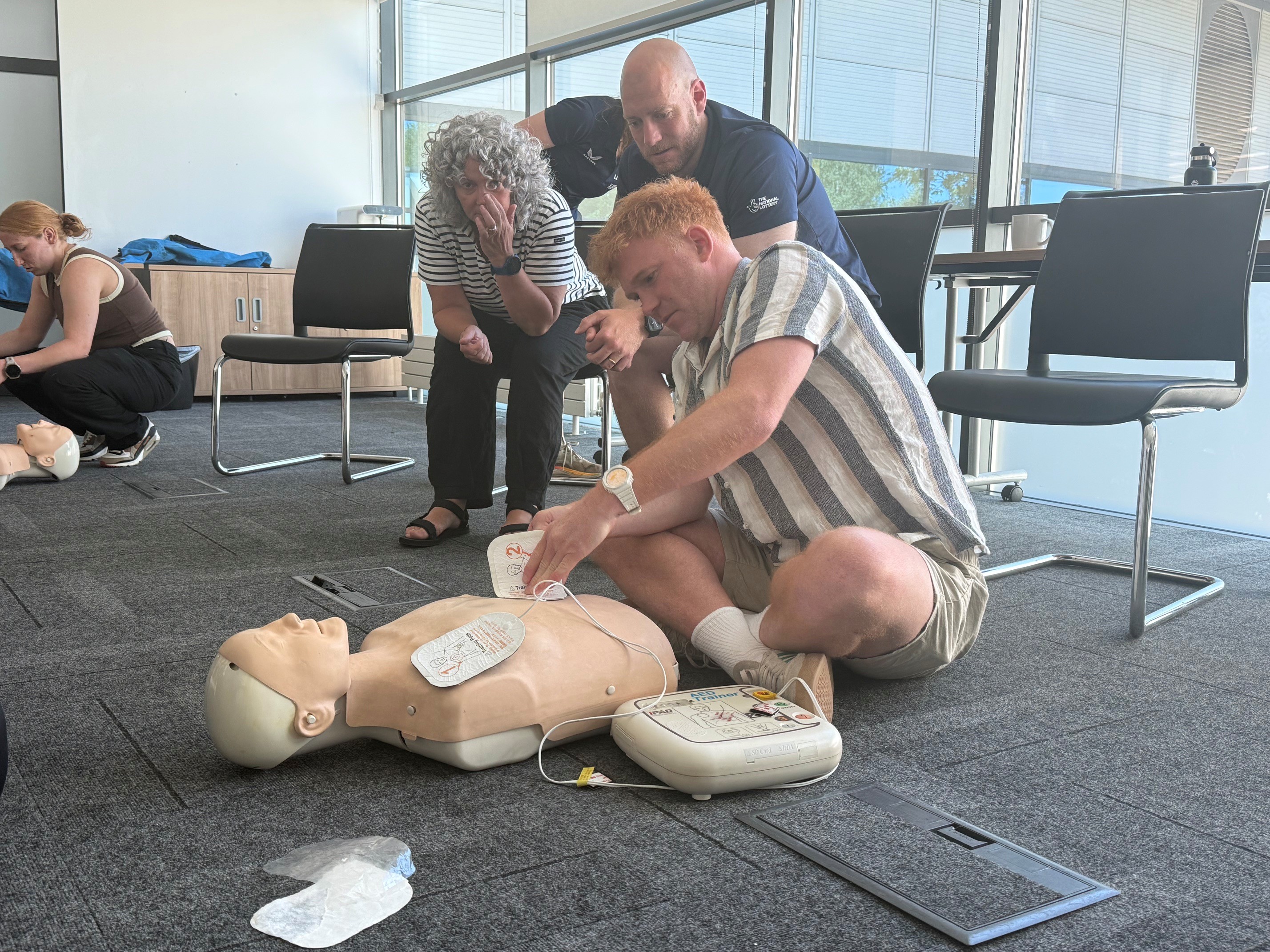 Participant uses an AED training device on a CPR manikin during a UK Coaching First Aid workshop attended by British Cycling staff and volunteers.