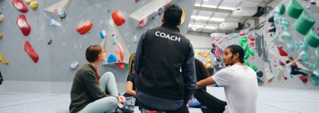 Coach talking to participants near a rock climbing wall