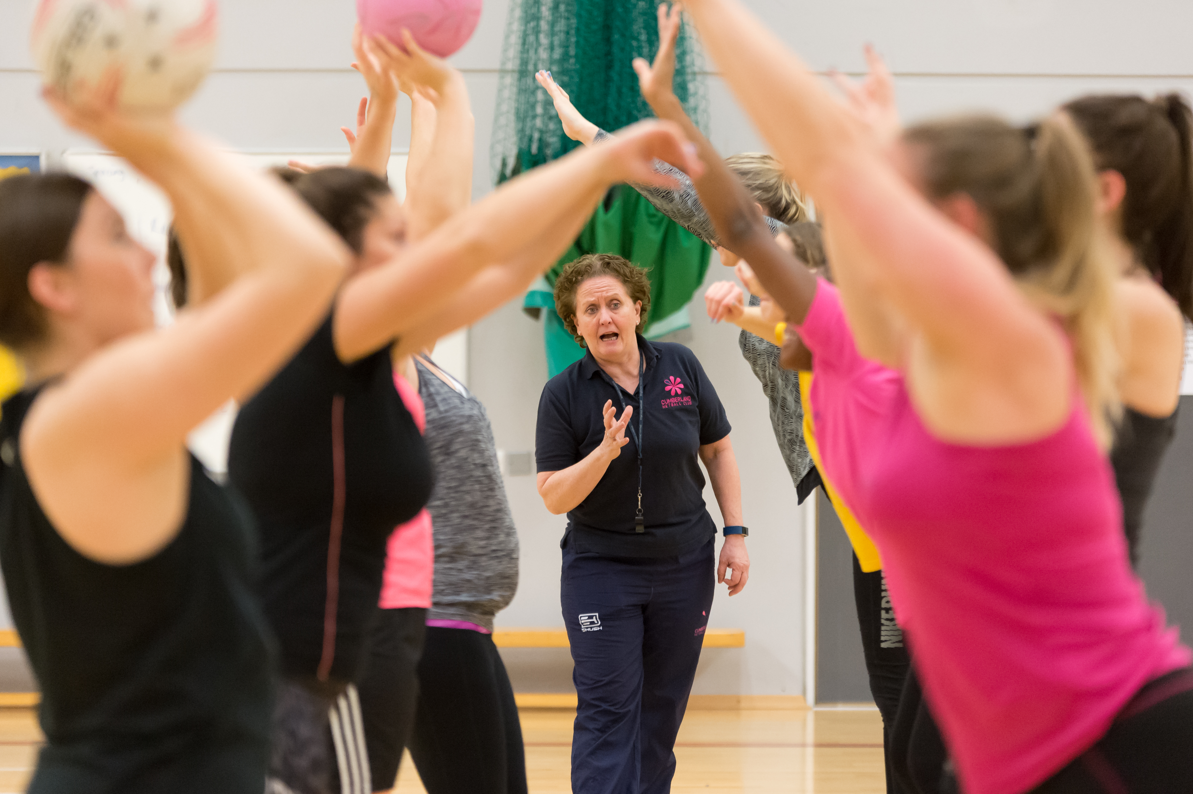 A netball coach is seen through a crowd of raised arms as she leads a session