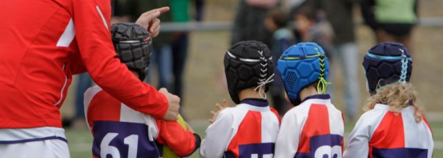 Coach standing with children wearing rugby gear and scrum caps