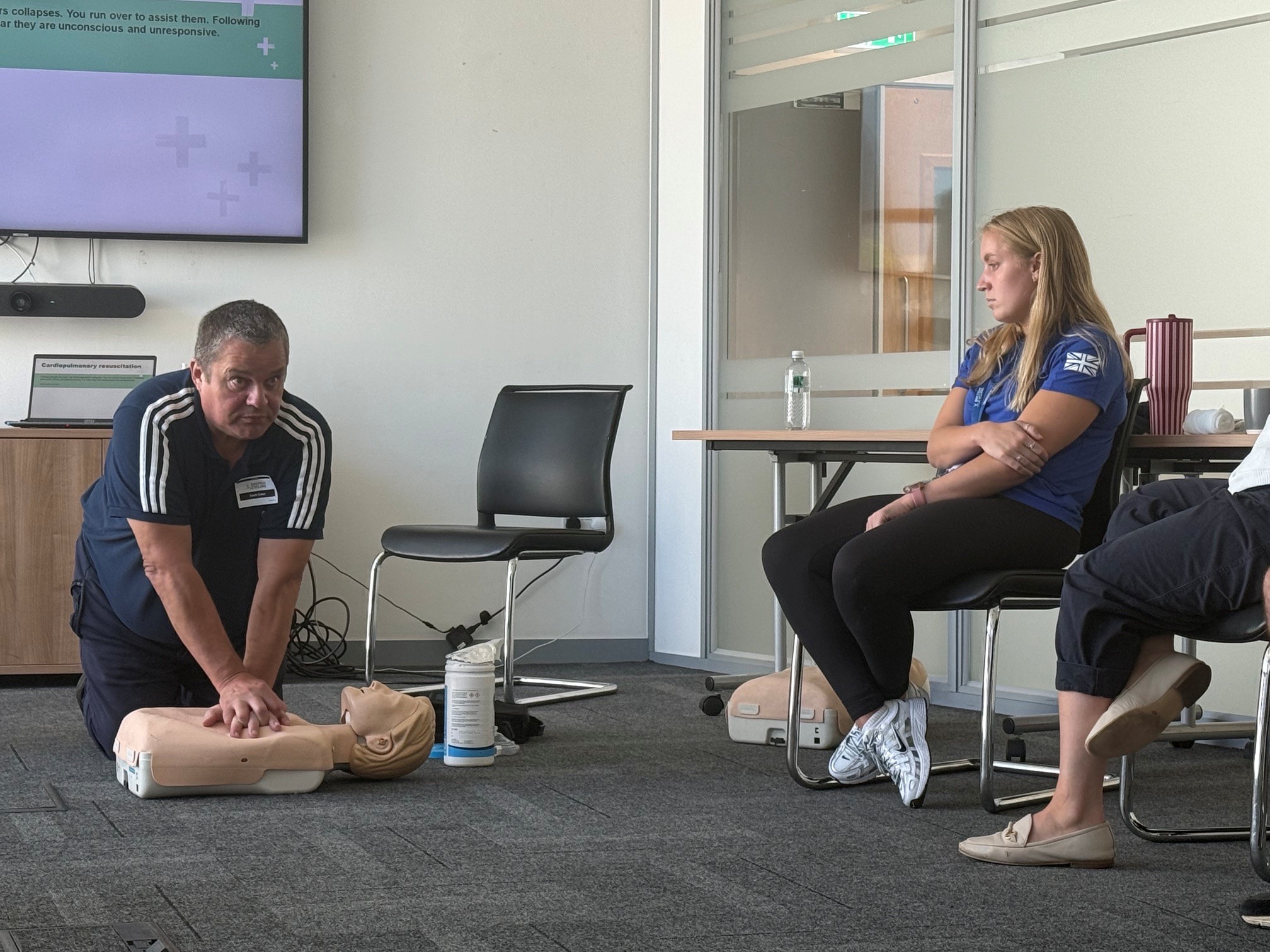 UK Coaching tutor demonstrates CPR techniques on a training manikin as participants observe during a First Aid in Sport and Physical Activity workshop at British Cycling's National Cycling Centre.