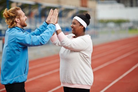 A smiling running coach and his participant exchange a congratulatory double high five on the running track, celebrating her achievement. 