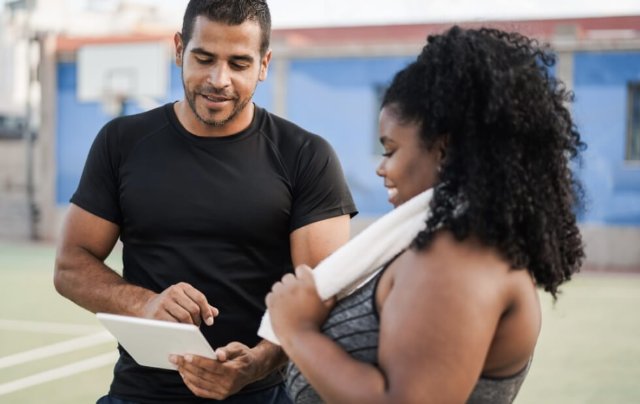 personal trainer talking to participant, showing her something on a tablet