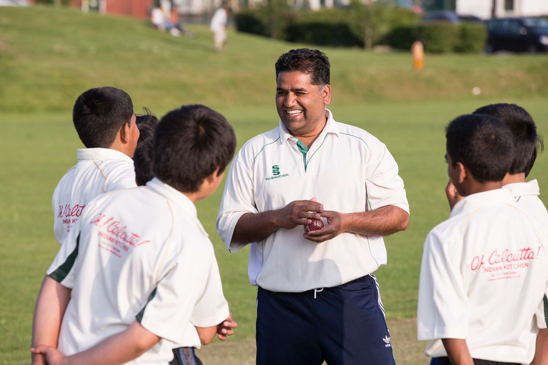 A group of children playing cricket gather around their coach. 